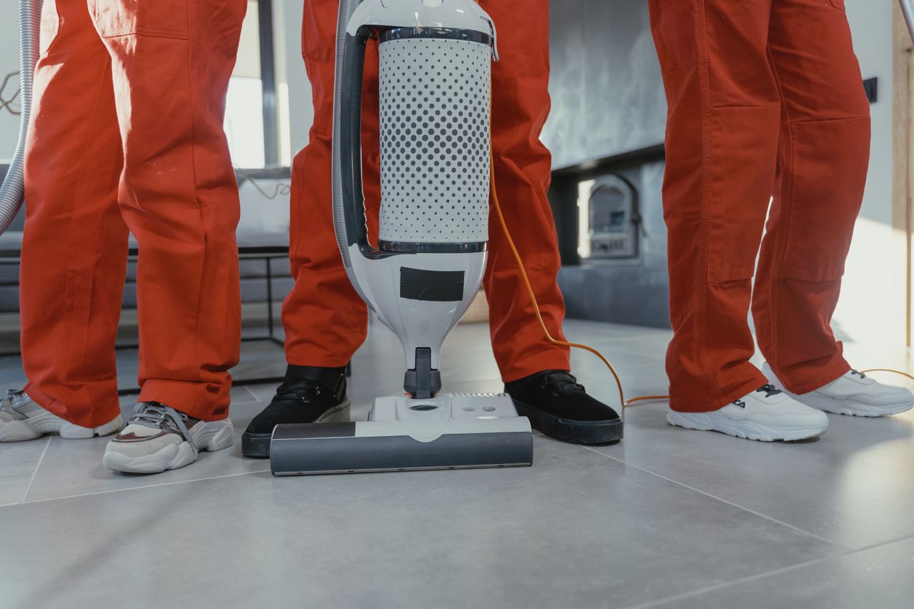 services-03 Team of professional cleaners in red uniforms using a vacuum cleaner indoors.